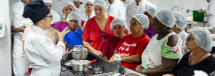 Mulheres de touca e avental em uma cozinha industrial durante a produção de chocolate