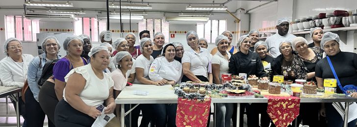 Turma da oficina de doces natalinos reunida atrás de uma bancada com os doces produzidos