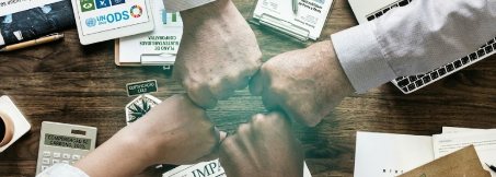 Mãos unidas sobre uma mesa com relatórios de sustentabilidade e material dos ODS