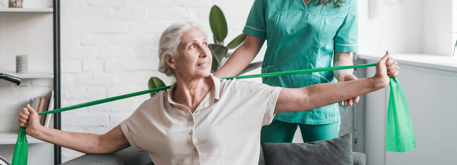 Fisioterapeuta acompanha idosa em exercício com faixa elástica em casa