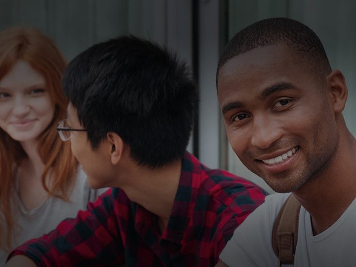 Três estudantes conversando e sorrindo em um corredor da universidade