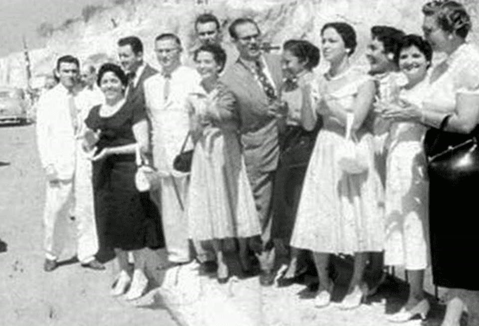 Grupo de professores e alunas posando enfileirados ao ar livre, em foto de arquivo em preto e branco