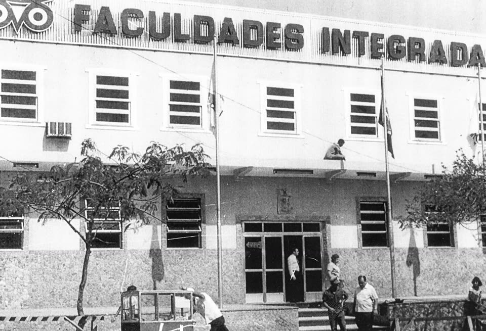 Fachada da sede em preto e branco, com o letreiro "Faculdades Integradas" e a coruja no alto