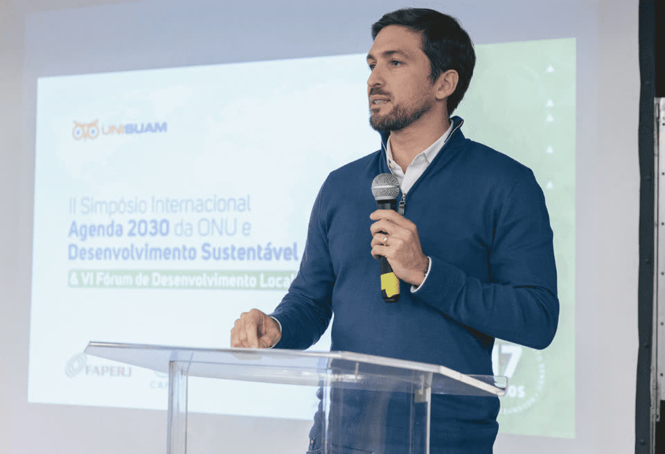 Pesquisador ao microfone em púlpito de acrílico durante o Fórum de Desenvolvimento Local