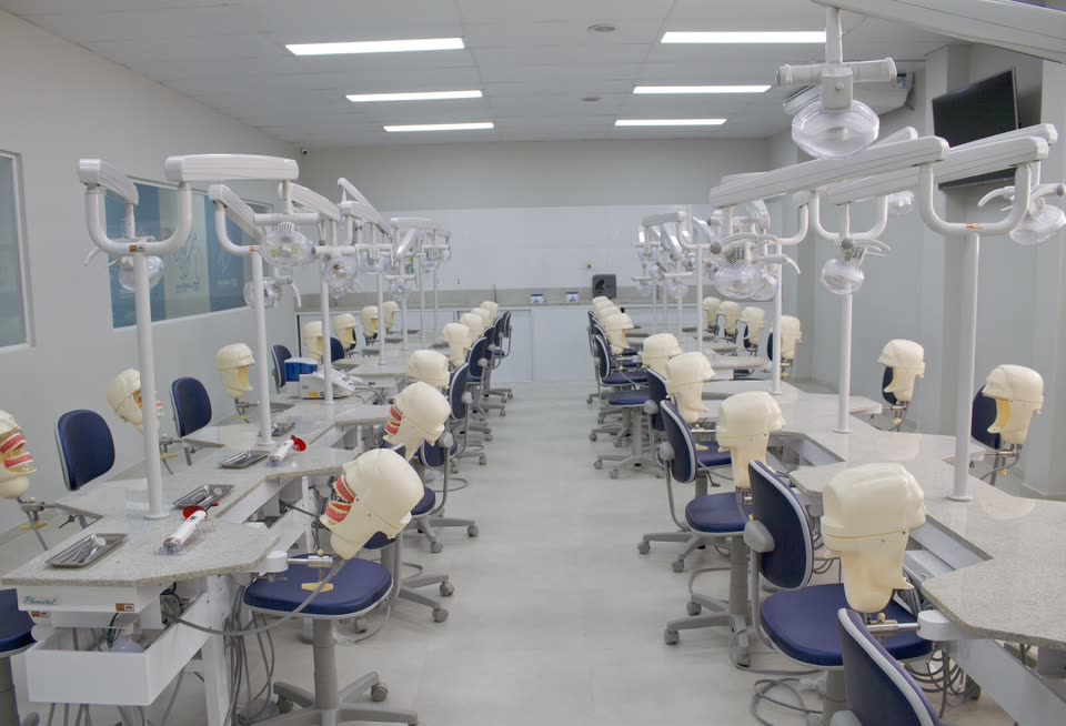 Laboratório de Odontologia com fileiras de bancadas, refletores e manequins de treino