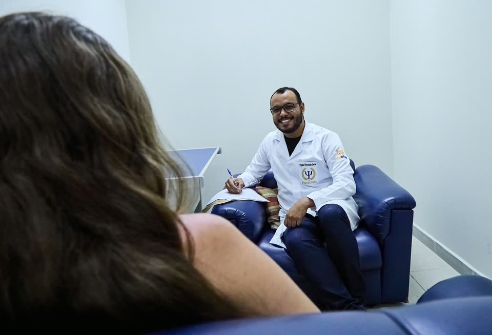 Psicólogo de jaleco anotando durante um atendimento na clínica-escola