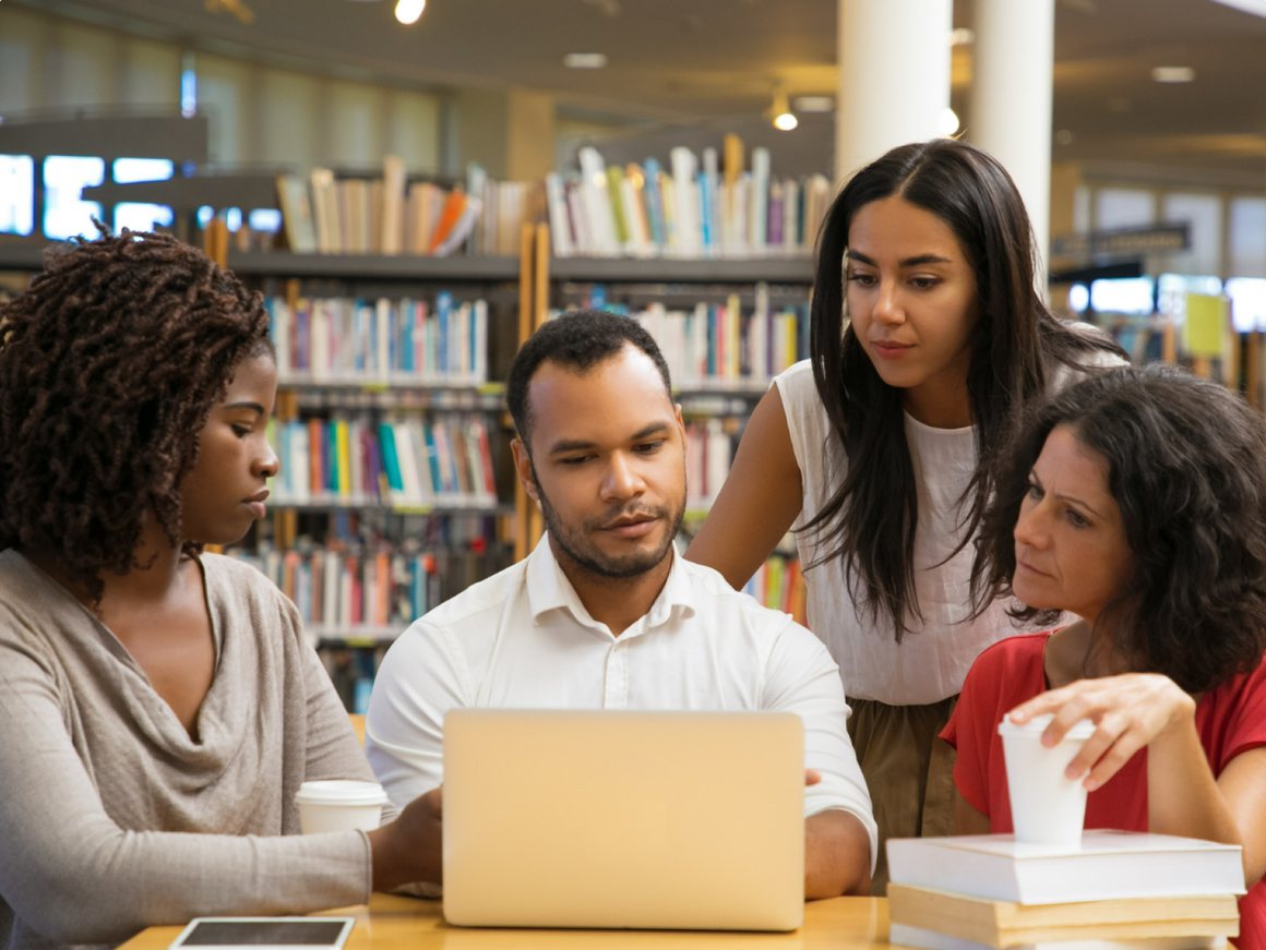 Grupo de estudantes pesquisando juntos em torno de um notebook na biblioteca