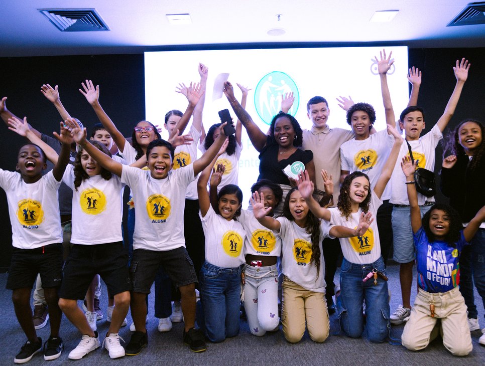 Crianças e educadores de projeto social da UNISUAM celebrando com os braços erguidos