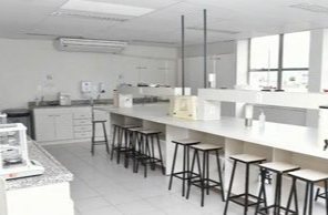 Laboratório de química com bancadas brancas e bancos altos