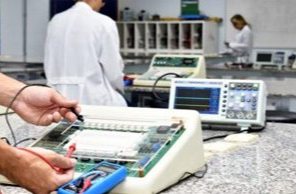 Estudantes de jaleco medindo circuitos em bancada de eletrônica