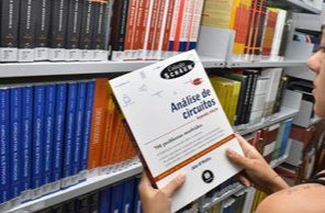 Estudante retirando um livro de análise de circuitos da estante