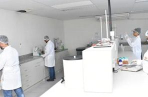 Estudantes de jaleco e touca trabalhando nas bancadas de um laboratório