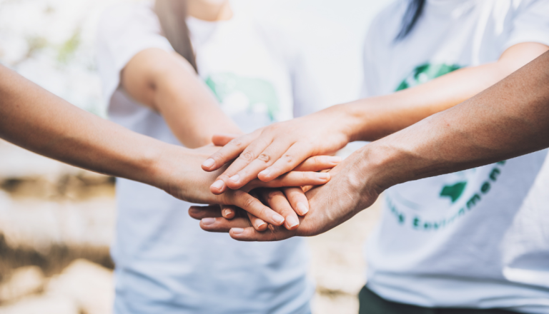 Pessoas reunidas em circulo com as mãos esticadas e juntas no centro do circulo.