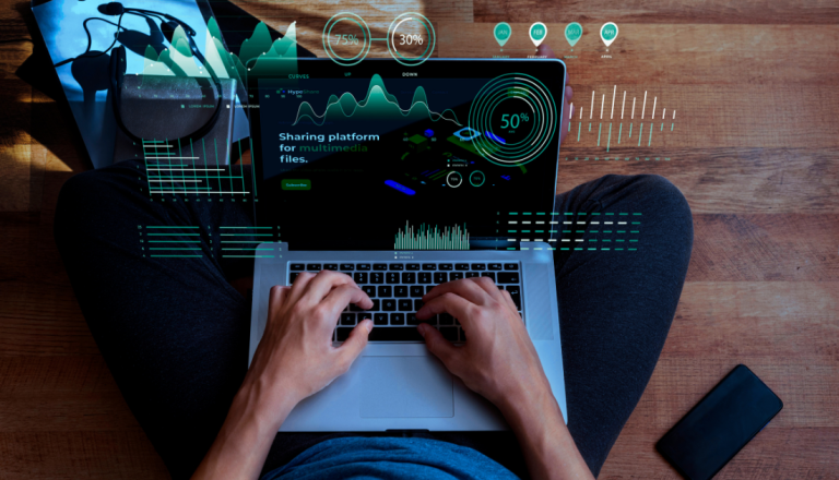 Uma pessoa sentada no chão e mexendo no notebook com dados e gráficos saindo na tela como 3D.