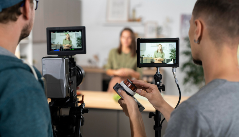 Dois cinegrafistas gravam uma mulher em ambiente interno usando câmeras profissionais com monitores externos durante uma produção de vídeo.