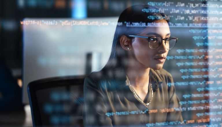 Mulher trabalhando em frente ao computador com códigos e dados projetados na tela, representando a atuação de profissionais da área de Ciência de Dados e tecnologia.