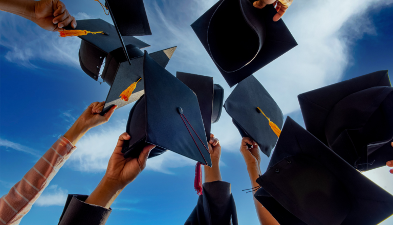 Estudantes erguem seus capelos de formatura em direção ao céu azul durante uma cerimônia de conclusão de curso, celebrando a conquista do diploma.