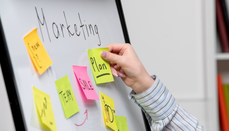 Pessoa organizando post-its em um quadro de planejamento estratégico com tópicos relacionados a marketing, vendas, equipe e finanças, representando a gestão de campanhas de marketing digital.