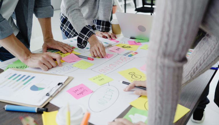 Equipe reúne-se em torno de uma mesa para planejar estratégias de negócios, utilizando post-its, gráficos e anotações durante uma sessão colaborativa.
