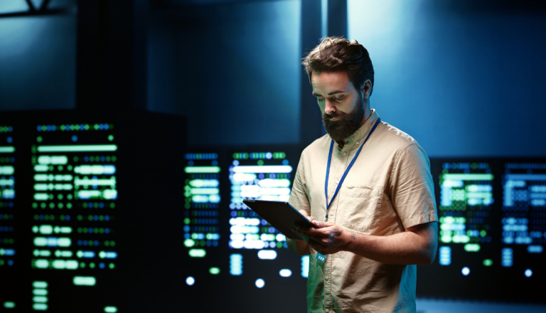 Profissional de Redes de Computadores utiliza um tablet para monitorar servidores em um data center com painéis de infraestrutura de rede ao fundo.