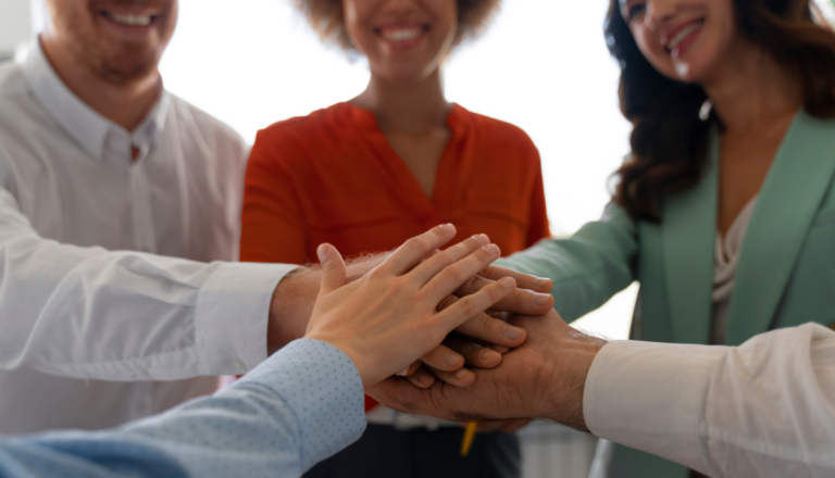 Grupo de pessoas une as mãos em um gesto de colaboração e trabalho em equipe durante uma atividade coletiva.