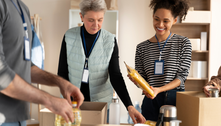 Grupo de voluntários organiza alimentos e itens de primeira necessidade em caixas durante uma ação social comunitária.